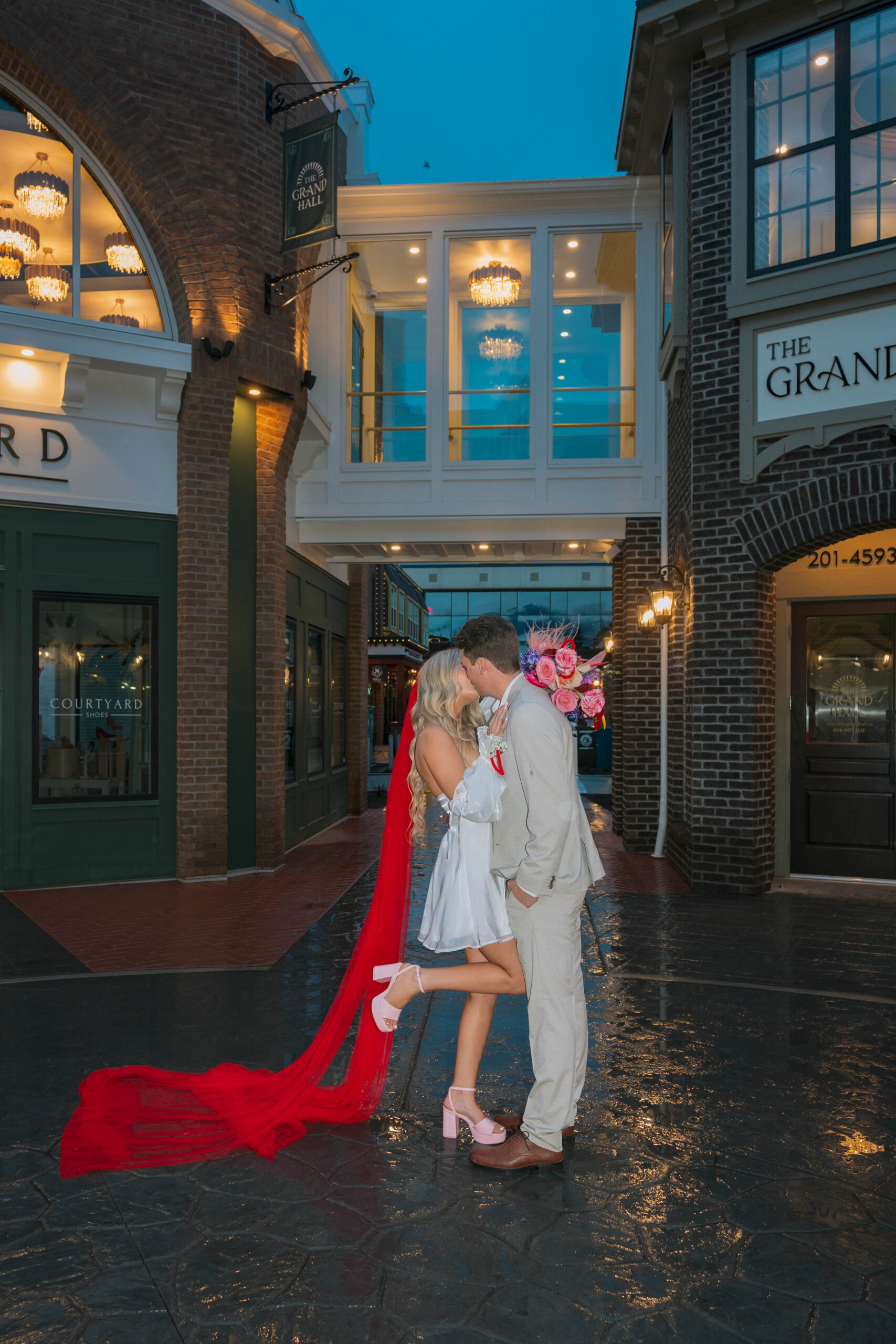 Bride and groom pose outside The Grand Hall Chilliwack at District 1881, surrounded by vintage-inspired storefronts and cobblestone streets.