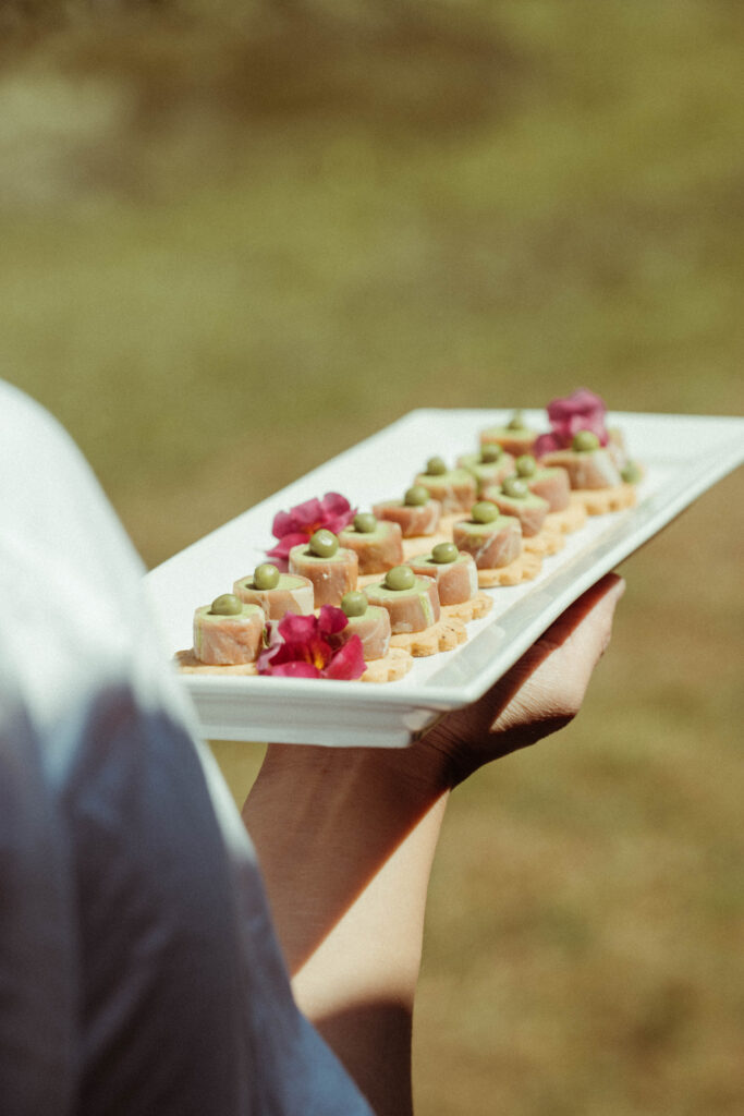 Passed appetizers decorated with small pink flowers at an outdoor event.
